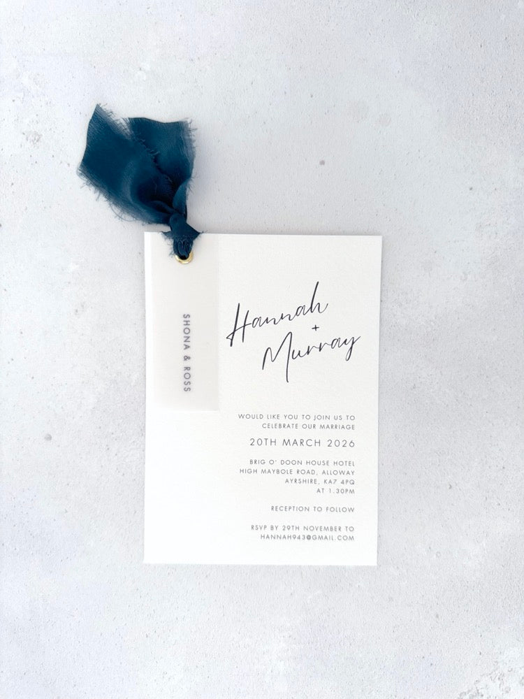 Navy Hannah wedding invite with vellum name tag, metal eyelet, and tied silk ribbon