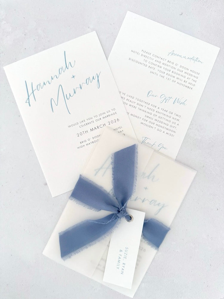 Pale blue Hannah wedding invitation with tied silk ribbon and transparent vellum jacket. Guest name tag with metal eyelet.  Insert card for wedding info and gift wishes