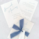 Pale blue Hannah wedding invitation with tied silk ribbon and transparent vellum jacket. Guest name tag with metal eyelet.  Insert card for wedding info and gift wishes