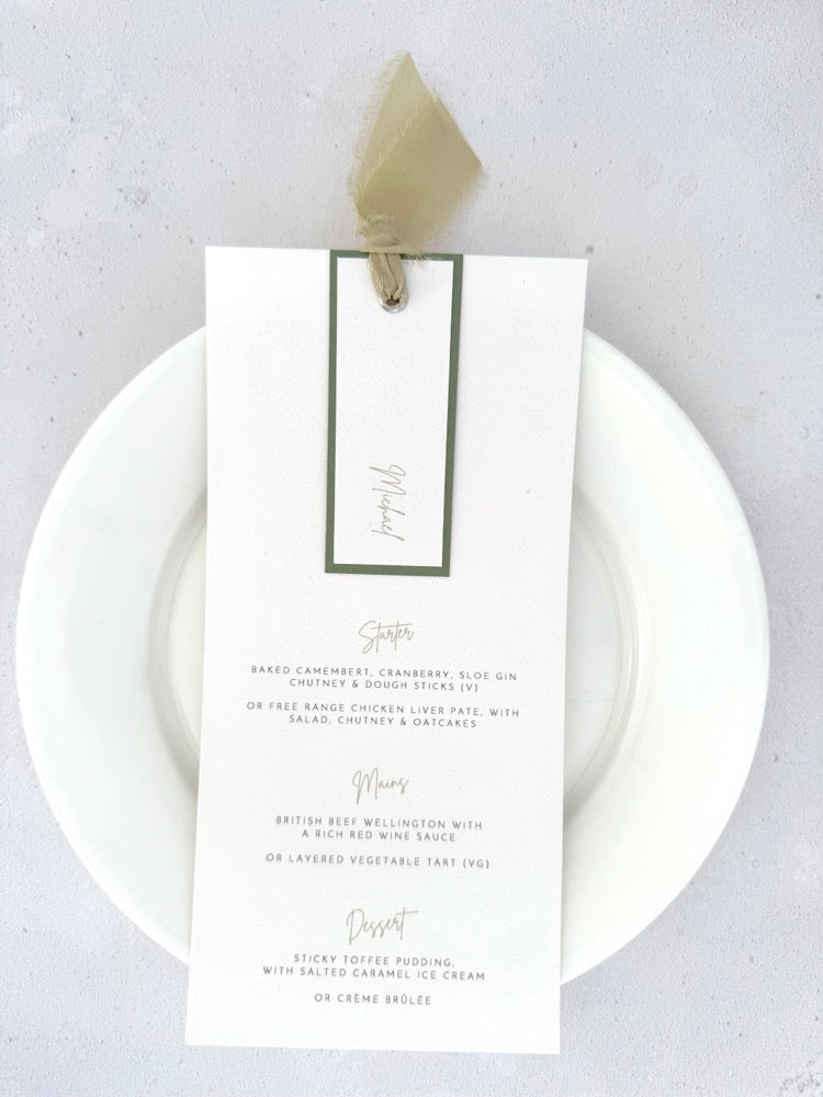 handmade Emma wedding menu with sage green silk ribbon, personalised name tag, and silver eyelet.