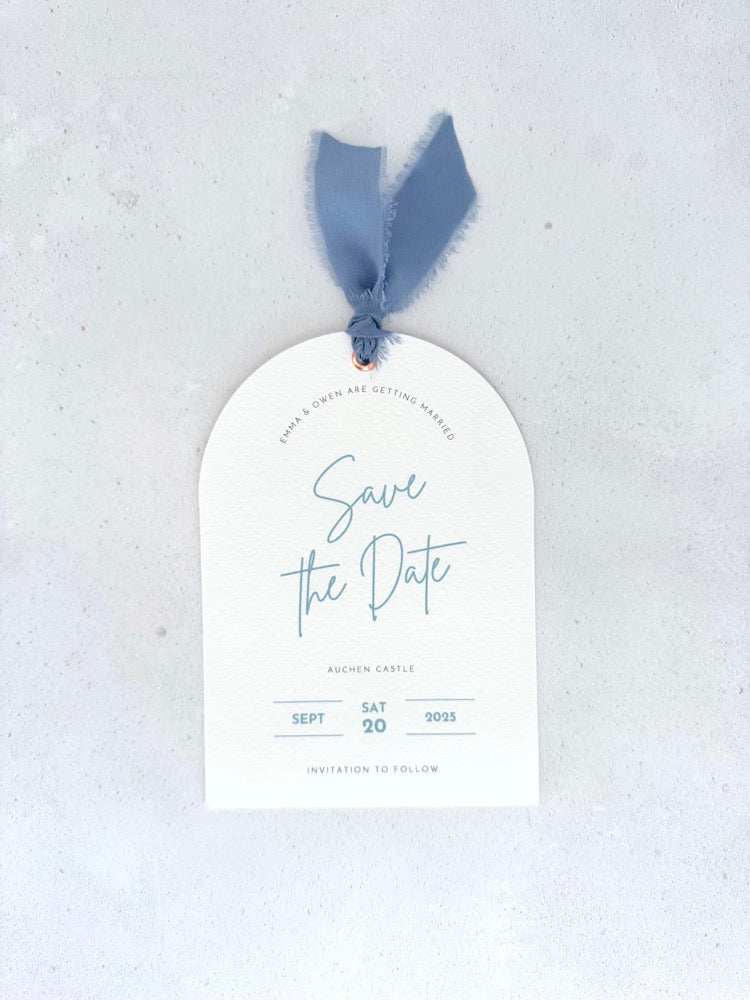 Textured white arched shaped save the date card with dusky cornflower blue ribbon and  metal eyelet Handmade by Zara Dumfries