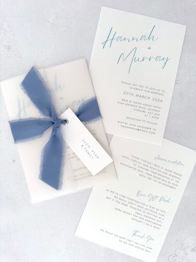 Dusky cornflower blue Hannah vellum wrap wedding invite with tied silk ribbon and guest name tag. Insert card for wedding info and menu options. Handmade by Zara Dumfries
