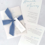 Dusky cornflower blue Hannah vellum wrap wedding invite with tied silk ribbon and guest name tag. Insert card for wedding info and menu options. Handmade by Zara Dumfries
