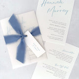 Dusky cornflower blue Hannah vellum wrap wedding invite with tied silk ribbon and guest name tag. Insert card for wedding info and menu options. Handmade by Zara Dumfries
