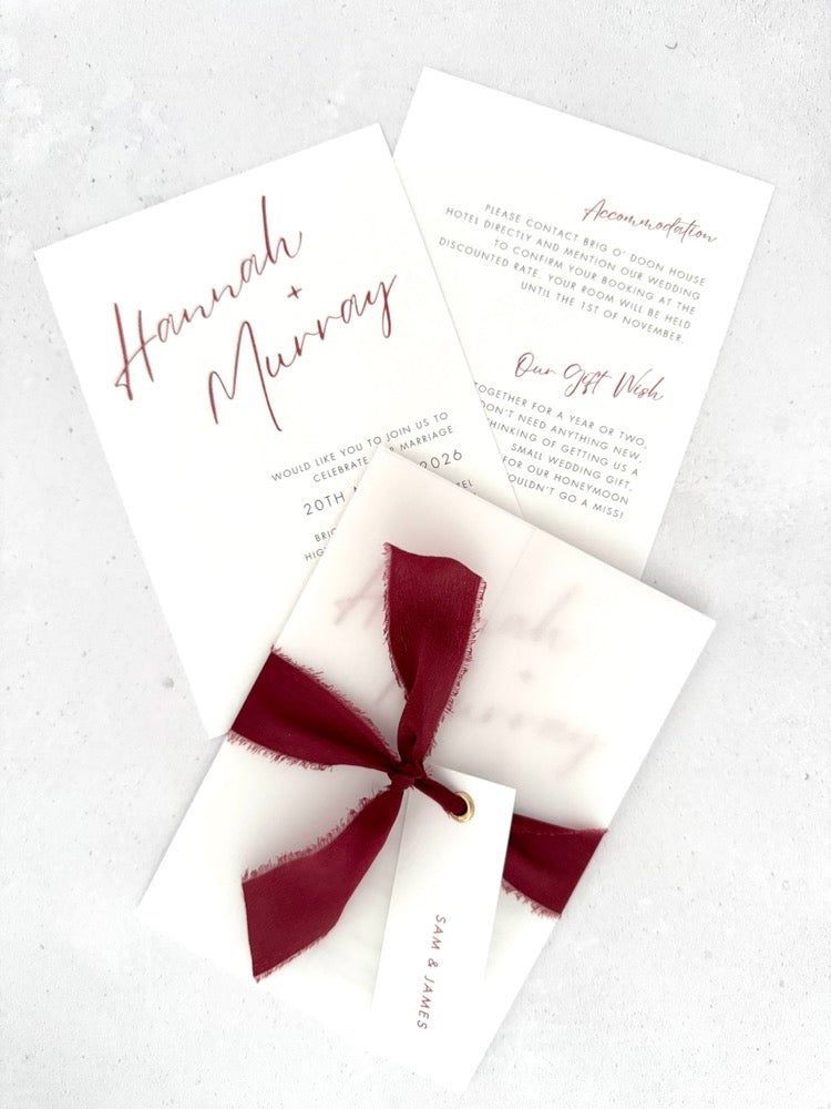 Burgundy Hannah wedding invitation with tied silk ribbon and transparent vellum jacket. Guest name tag with metal eyelet.  Insert card for wedding info and menu options. 