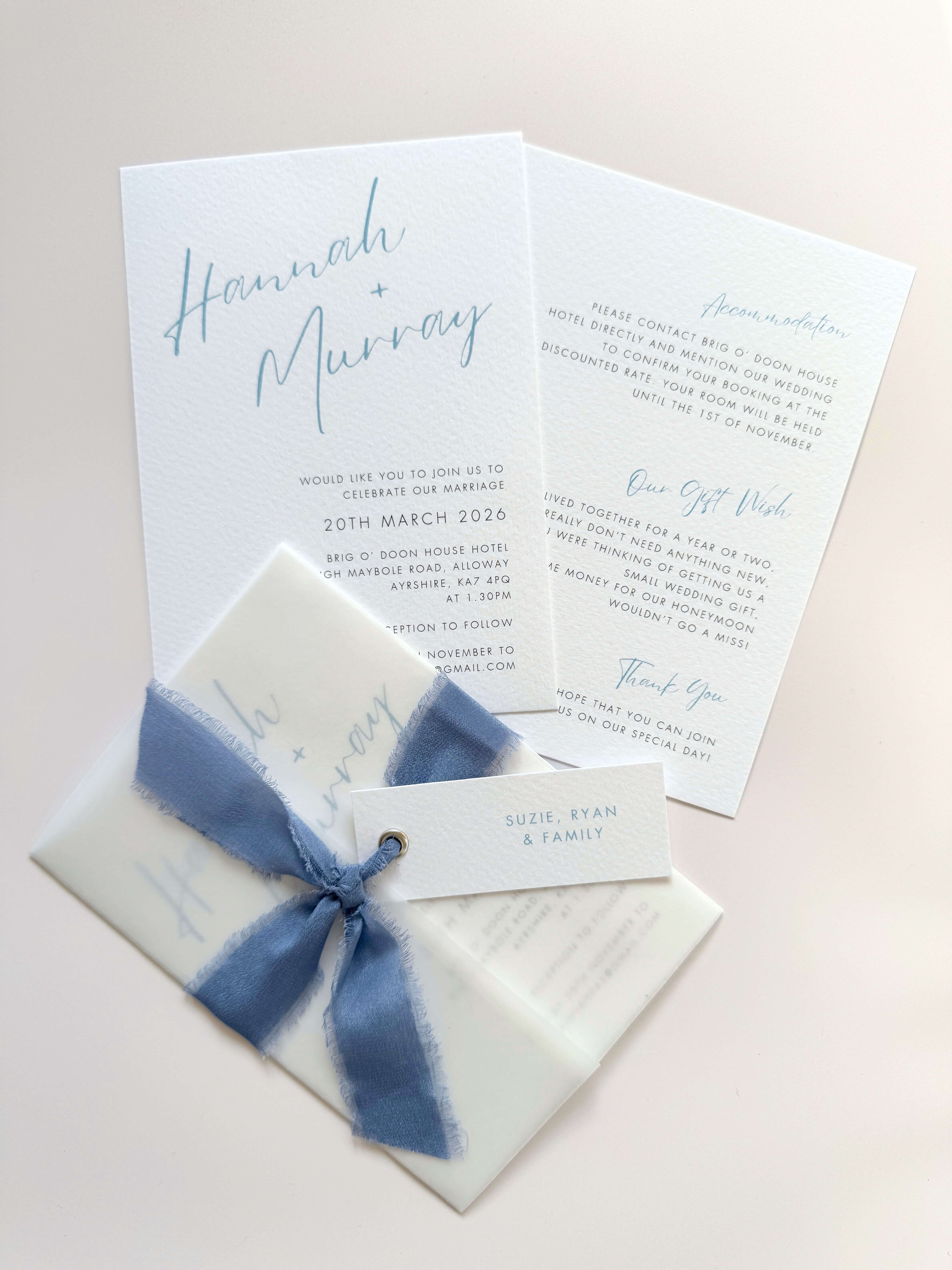 Pale blue Hannah wedding invitation with tied silk ribbon and transparent vellum jacket. Guest name tag with metal eyelet.  Insert card for wedding info and gift wishes