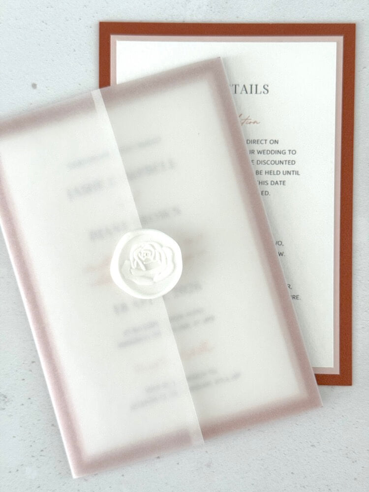 Layered wedding invitation held in a vellum wrap secured white rose wax seal