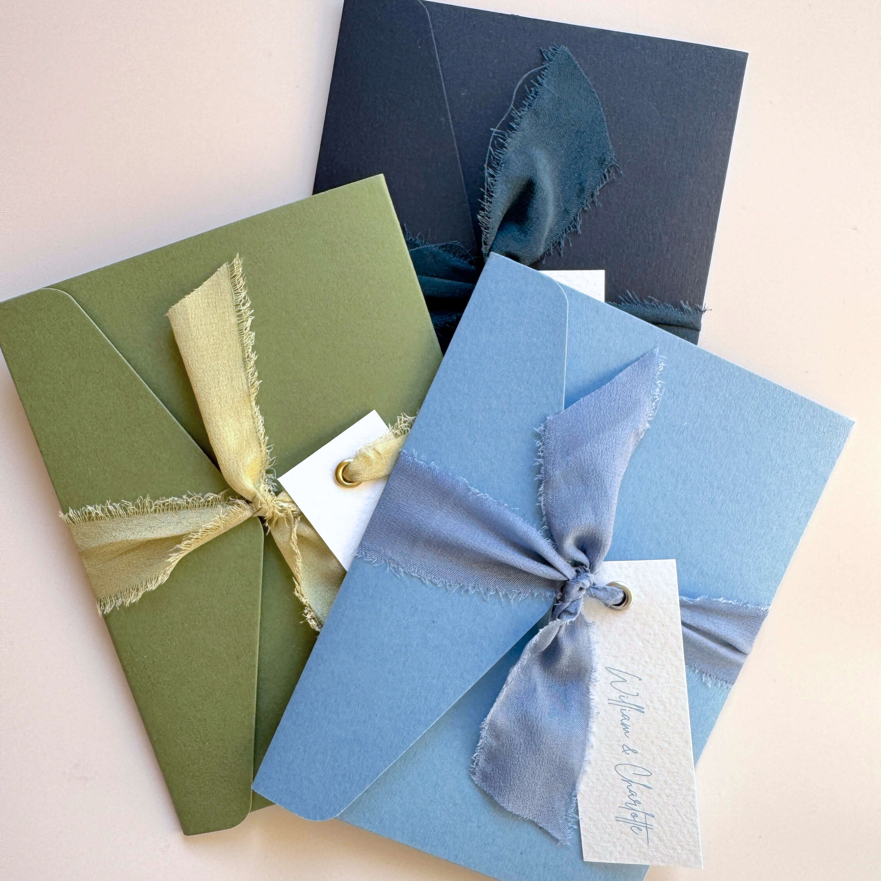 emma pocketfold wedding invites with silk ribbons and guest name tags in navy, sage green, and dusty cornflower blue