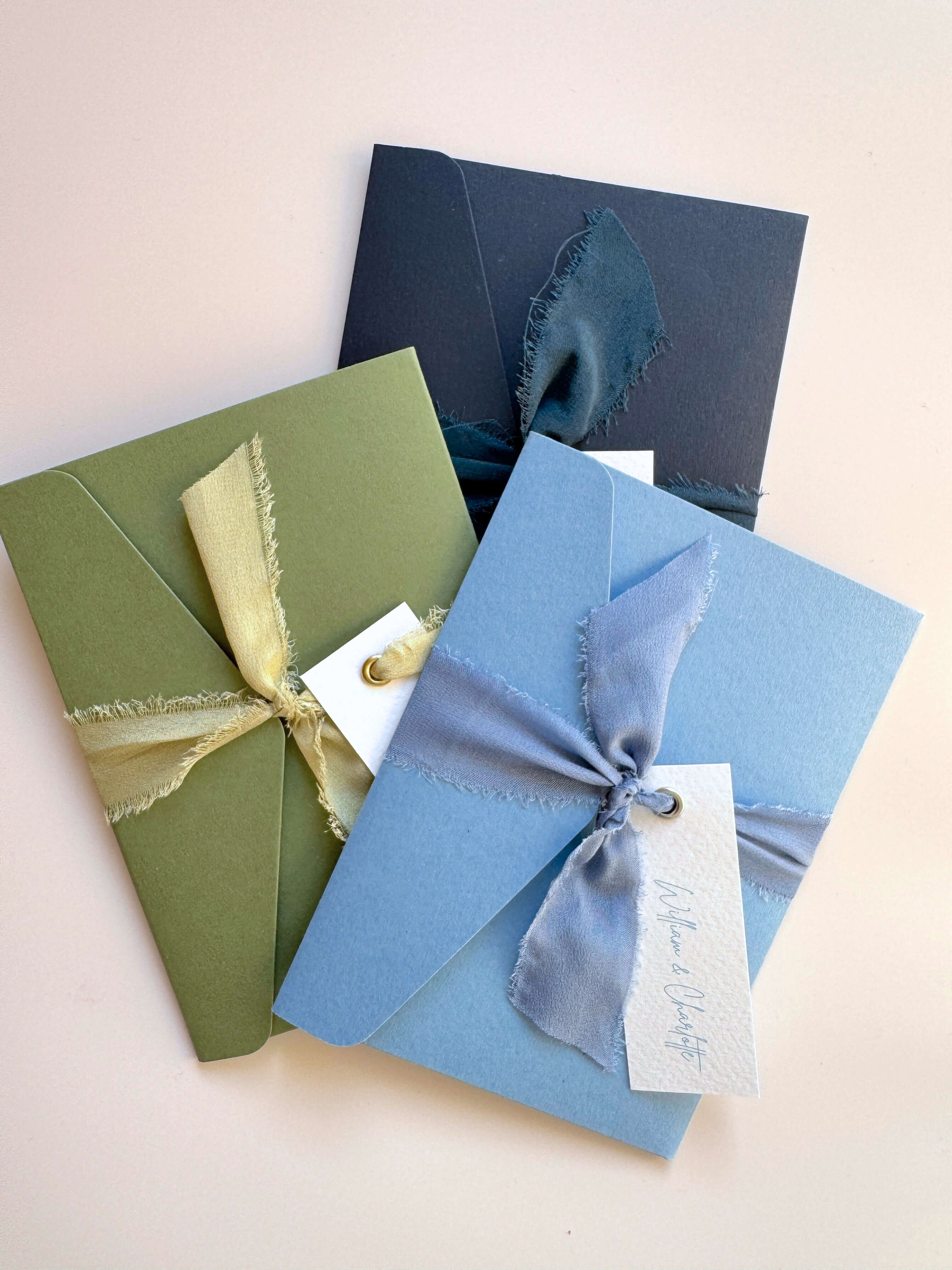 emma pocketfold wedding invites with silk ribbons and guest name tags in navy, sage green, and dusty cornflower blue