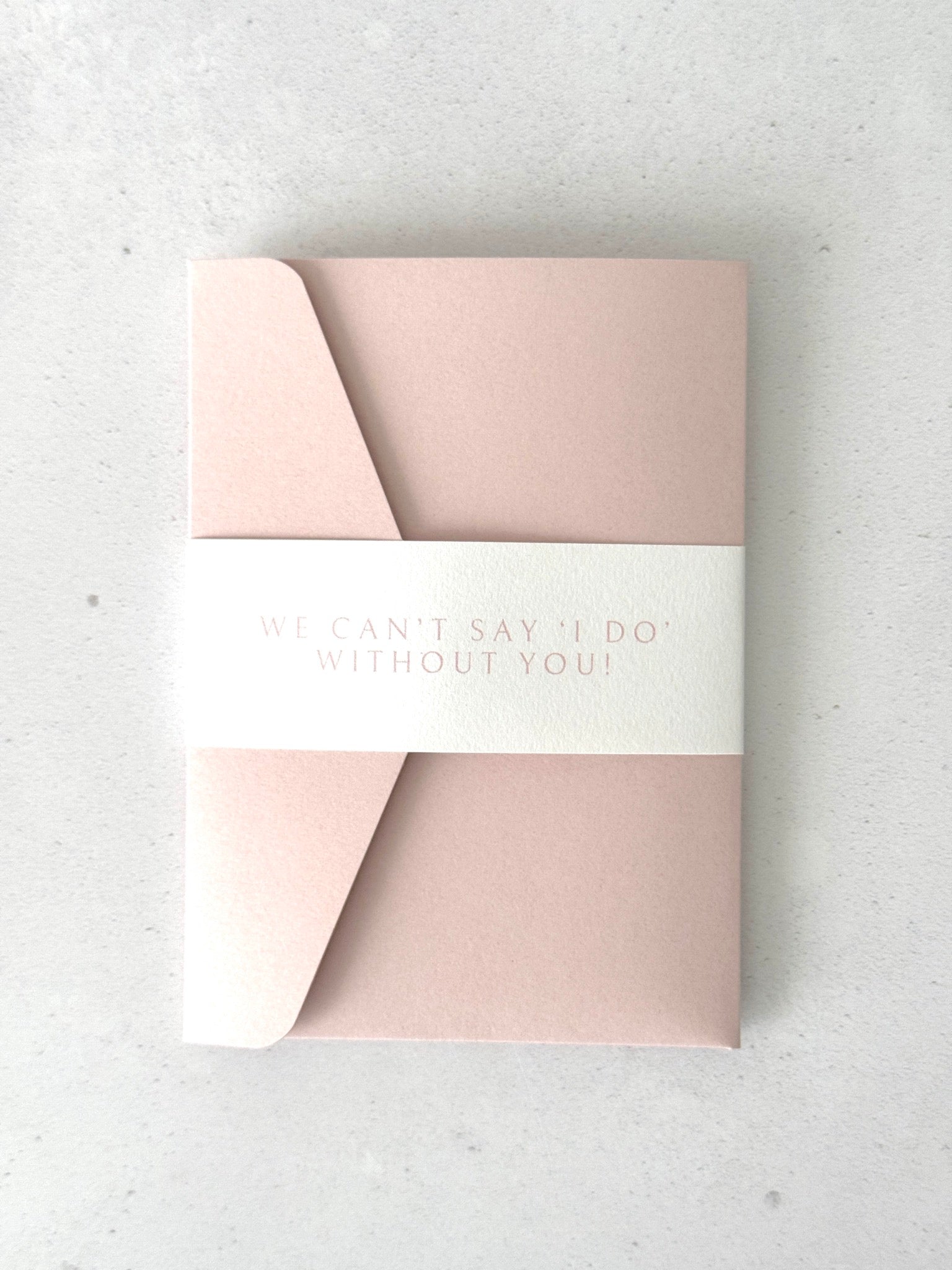 blush pink pocket wedding invite with "we can't say 'I Do' without you" personalised belly band