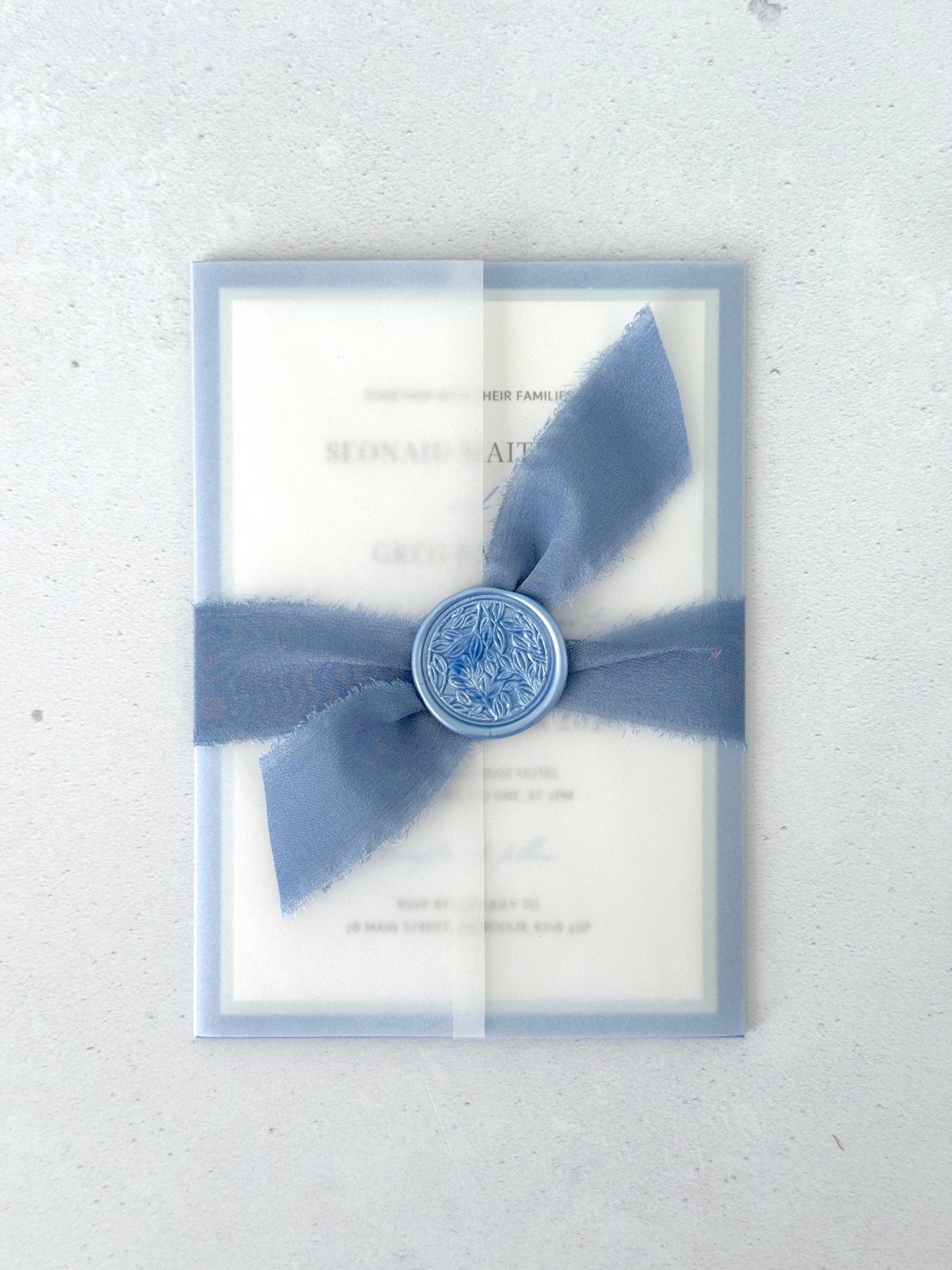 Transparent vellum wedding invite in dusty blue with tied silk ribbon and wax seal