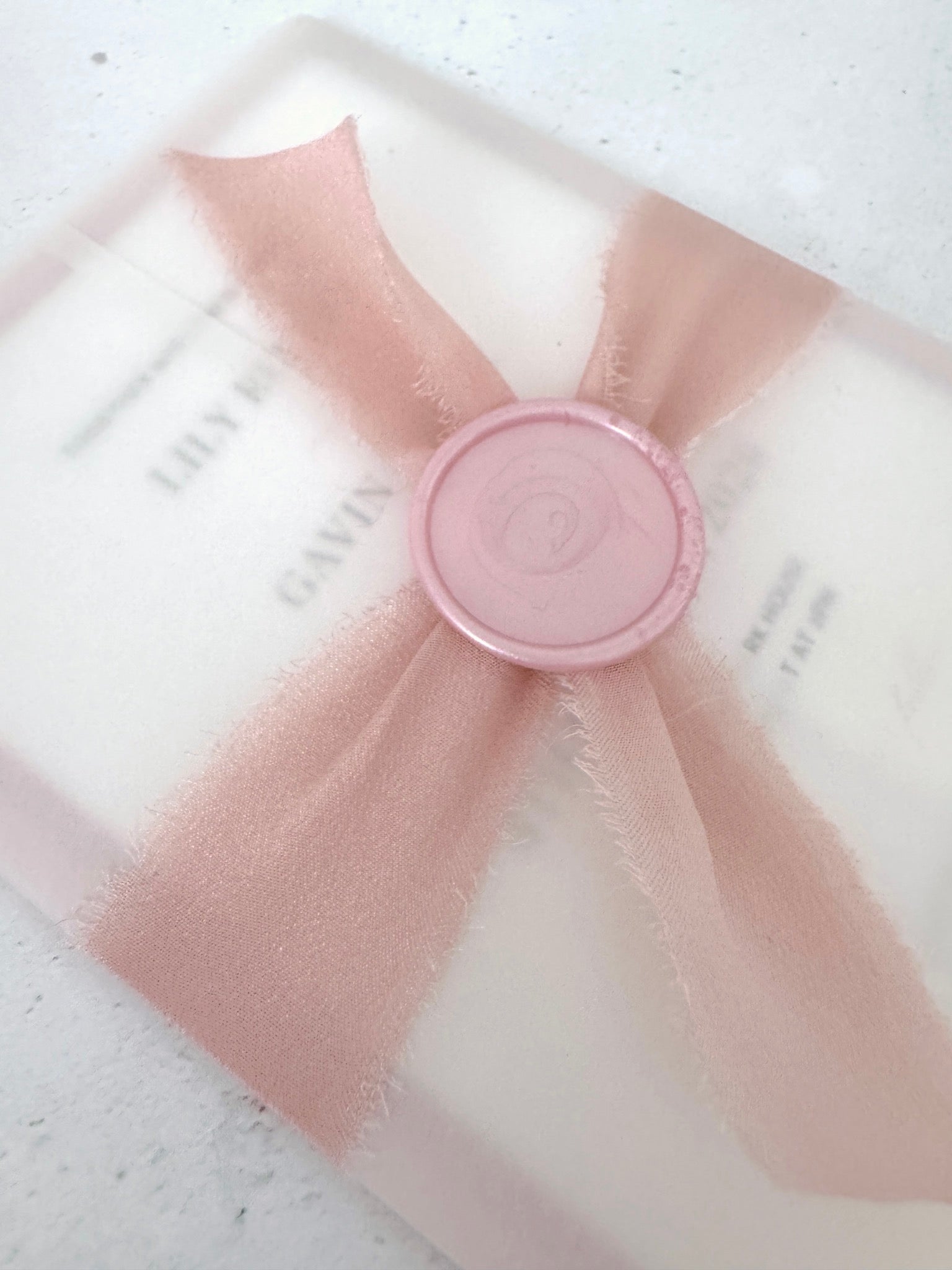 Tied silk ribbon with wax seal on see through paper wrapped wedding invite