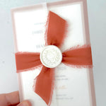 terracotta orange silk ribbon with pearl wax seal tied around a vellum wrapped wedding invite