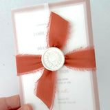 terracotta orange silk ribbon with pearl wax seal tied around a vellum wrapped wedding invite