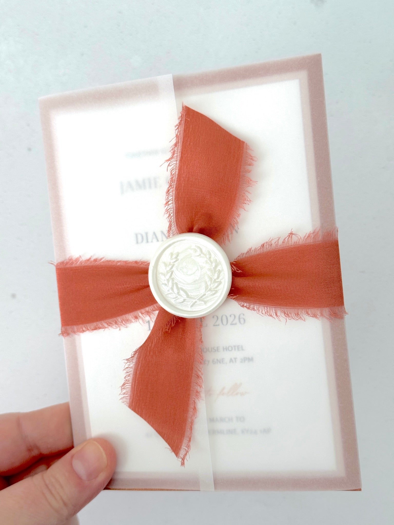 terracotta orange silk ribbon with pearl wax seal tied around a vellum wrapped wedding invite