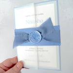 Lyn vellum wrap wedding invite with dusky blue belly band, silk ribbon, and waxs seal