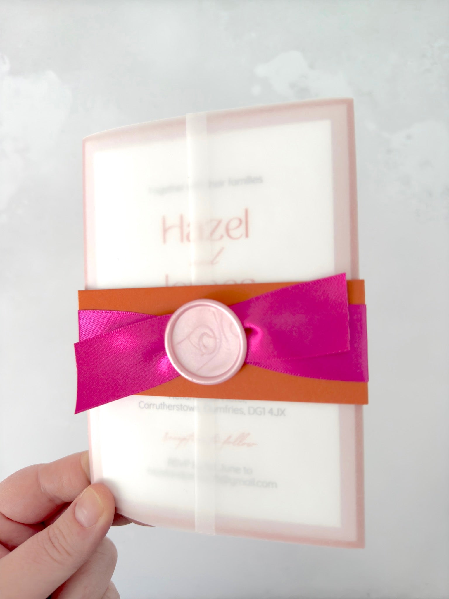 Lyn wedding invite with rust orange belly band and bright pink satin ribbon, pink wax seal, in a vellum wrap