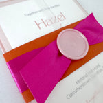 Fuschia pink satin ribbon, pink wax seal and orange belly band with transparent vellum sleeve 