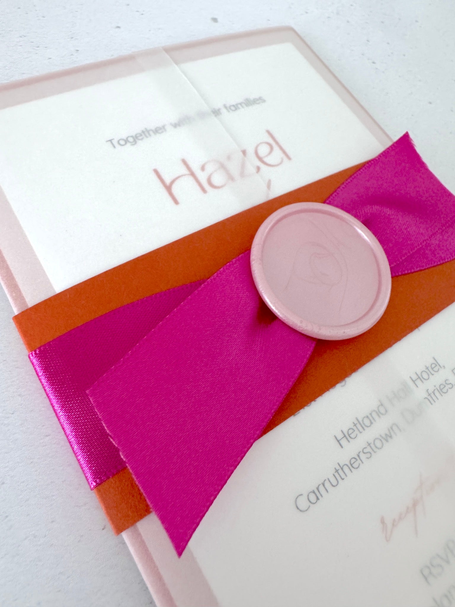 Fuschia pink satin ribbon, pink wax seal and orange belly band with transparent vellum sleeve 