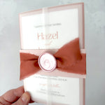 Lyn vellum jacket wedding invite with pink belly band and wax seal, and a terracotta orange silk ribbon