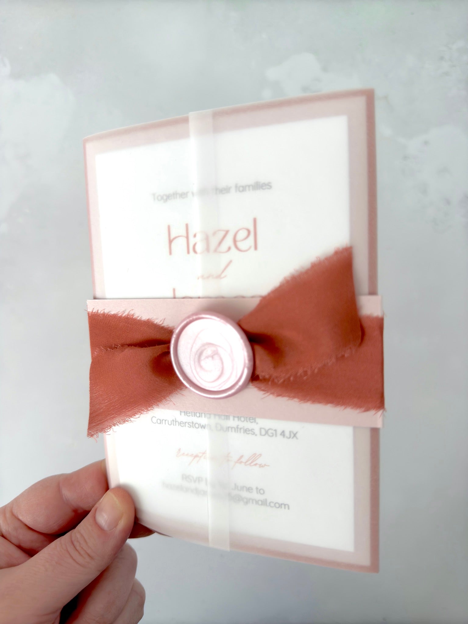 Lyn vellum jacket wedding invite with pink belly band and wax seal, and a terracotta orange silk ribbon