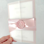 Pink handmade wedding invite with vellum sleeve and belly band with ribbon and wax seal