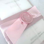 misty rose pink belly band with satin ribbon and wax seal vellum wrap wedding invite